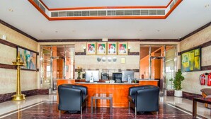 A hotel lobby with a marble floor, a reception desk, two black leather chairs, framed portraits on the wall, and a large potted plant. - OYO 231 Holiday Arabian Resort (Sayh Mudayrah)