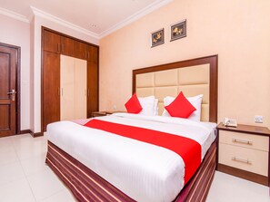 A hotel room with a large bed, a wooden wardrobe, a bedside table with a phone, and a wall-mounted light switch. - OYO 231 Holiday Arabian Resort (Sayh Mudayrah)