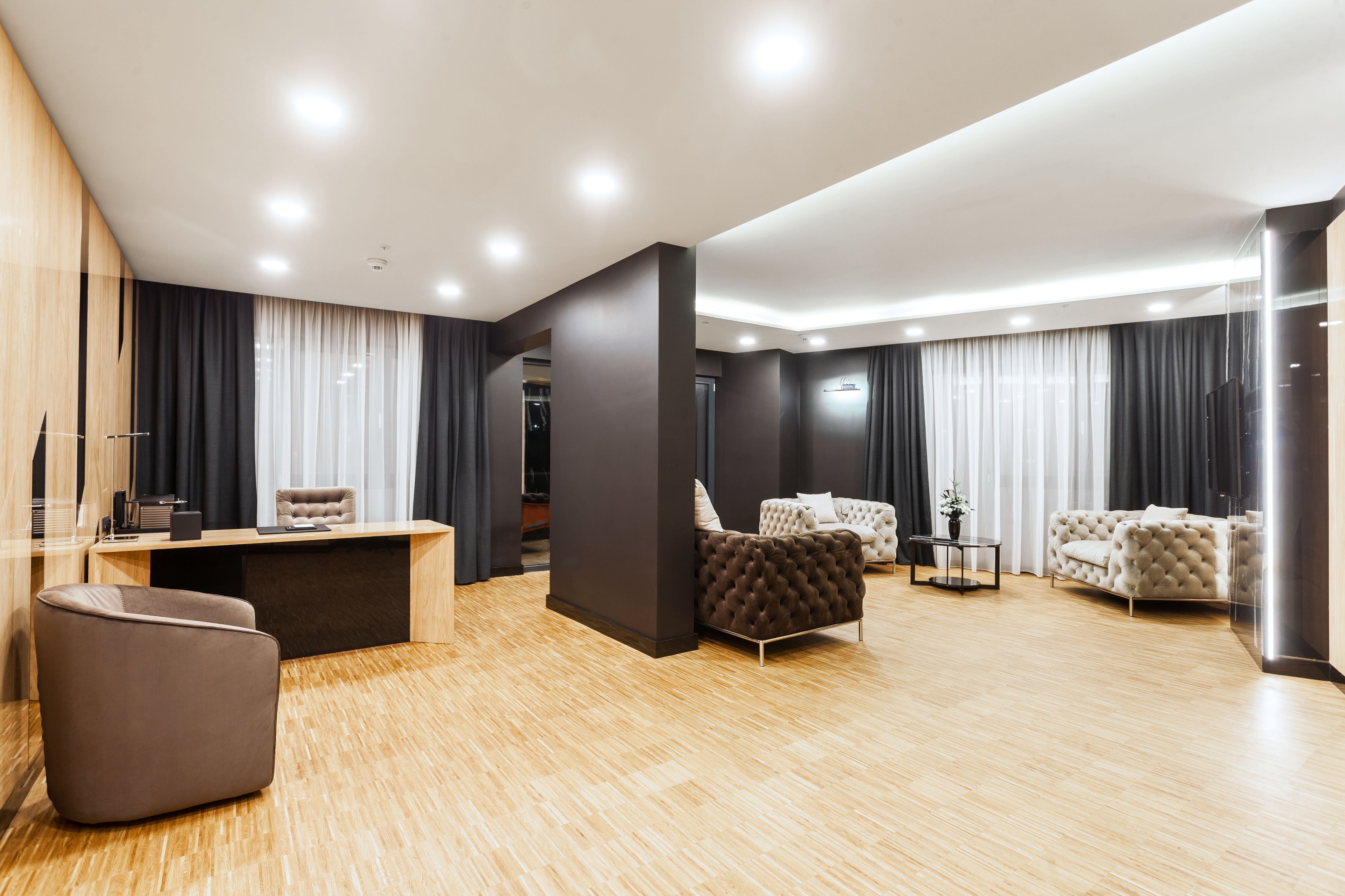 Uma sala de estar moderna com piso de madeira, um sofá, uma poltrona e uma escrivaninha com um computador.