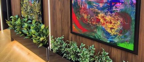 Two large abstract paintings on a wooden wall, a plant shelf below, and a wooden floor.