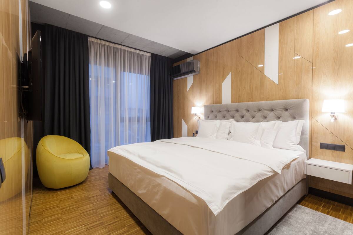A modern bedroom with a large bed, a yellow bean bag chair, and a wooden wall panel.