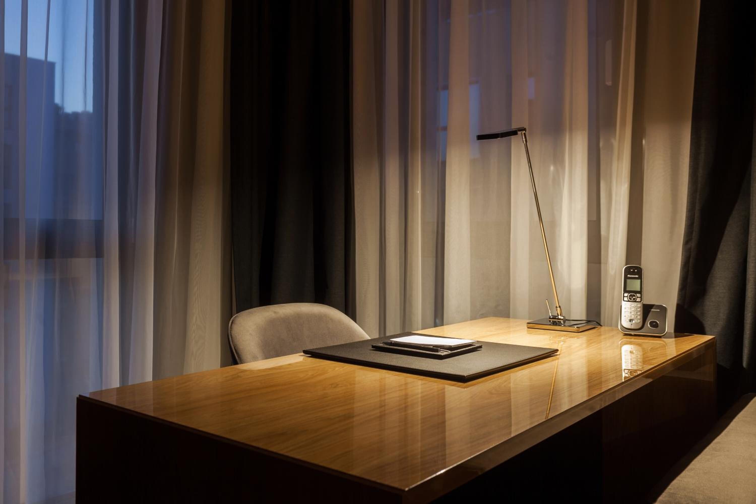 Een moderne hotelkamer met een houten bureau, een stoel, een bureaulamp en een telefoon.