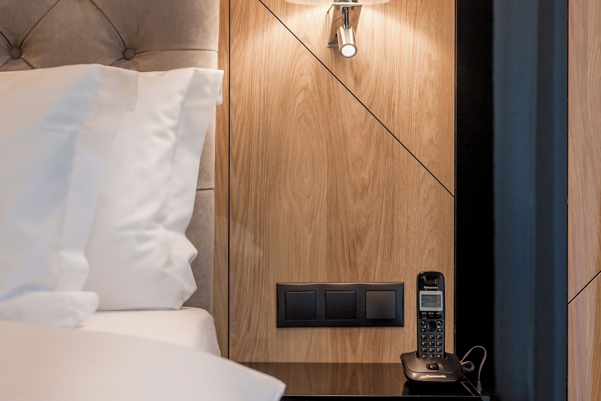 A hotel room with a tufted headboard, a bedside lamp, a control panel, and a telephone.
