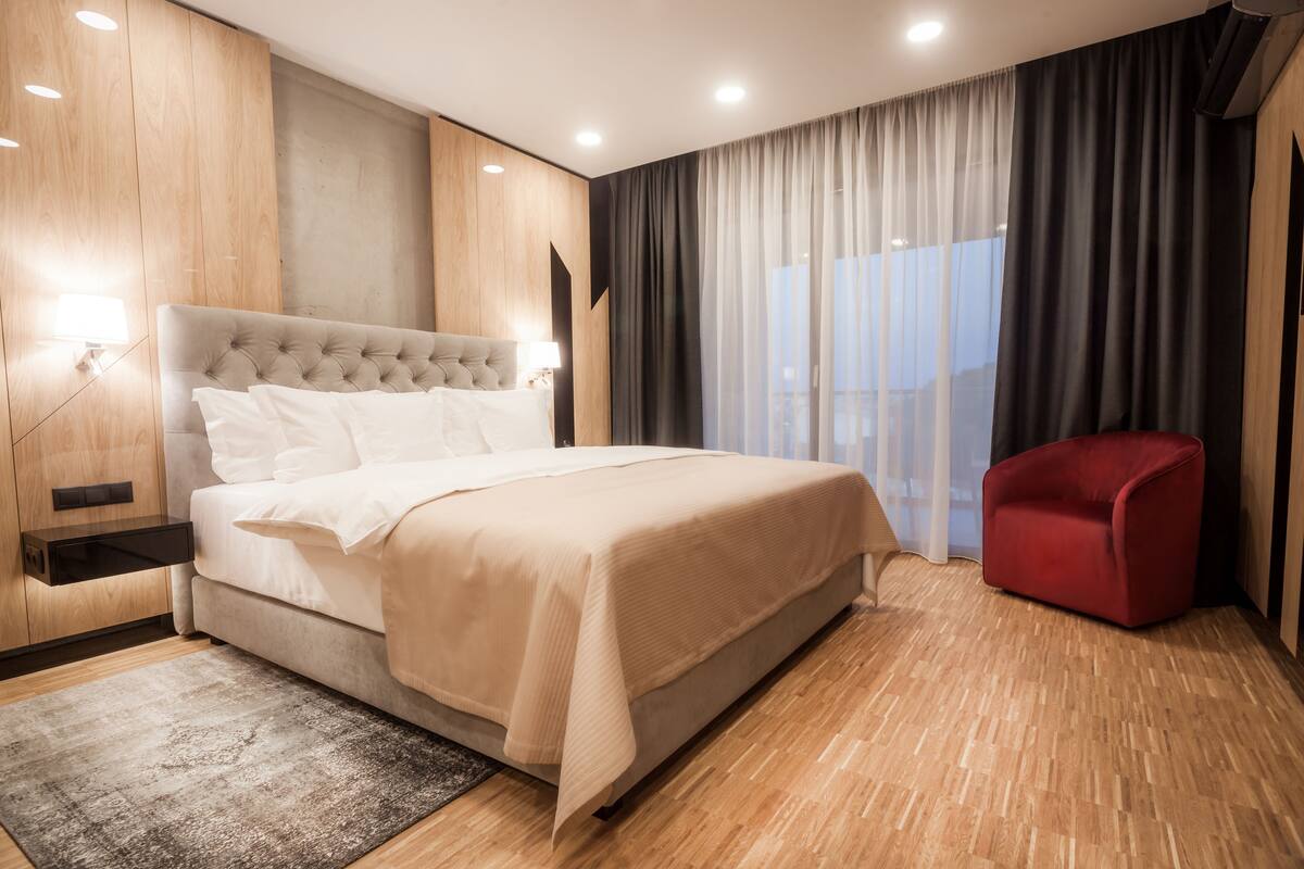 A modern bedroom with a large bed, a red chair, and a view of the outdoors.