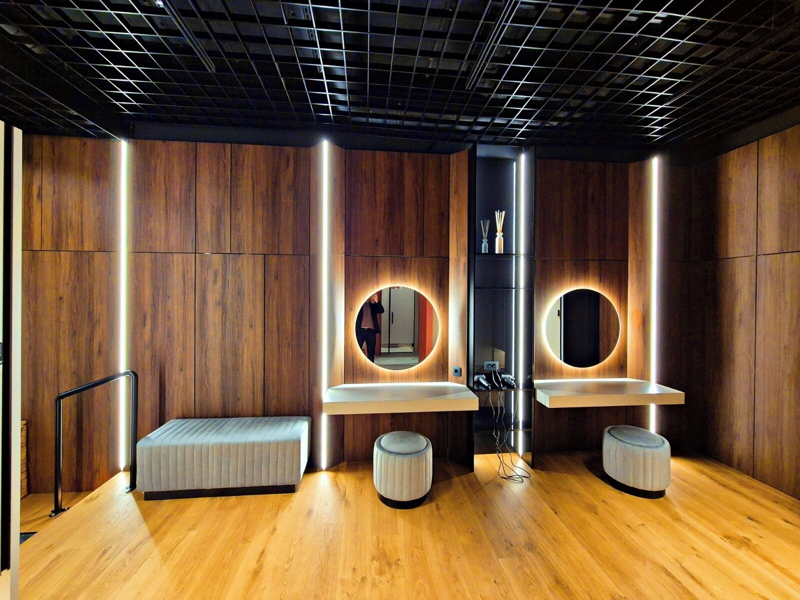A modern bathroom with wooden paneling, two sinks with round mirrors, and a bench.