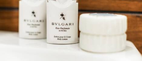 Tres botellas de loción corporal y perfume BVLGARI sobre una superficie blanca.