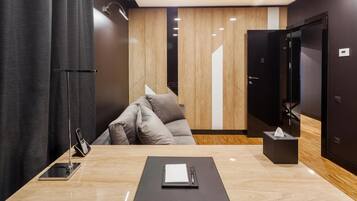 Une chambre d’hôtel moderne avec un plancher en bois, un canapé, un bureau avec un téléphone et un bloc-notes, et une porte dotée d’un miroir.