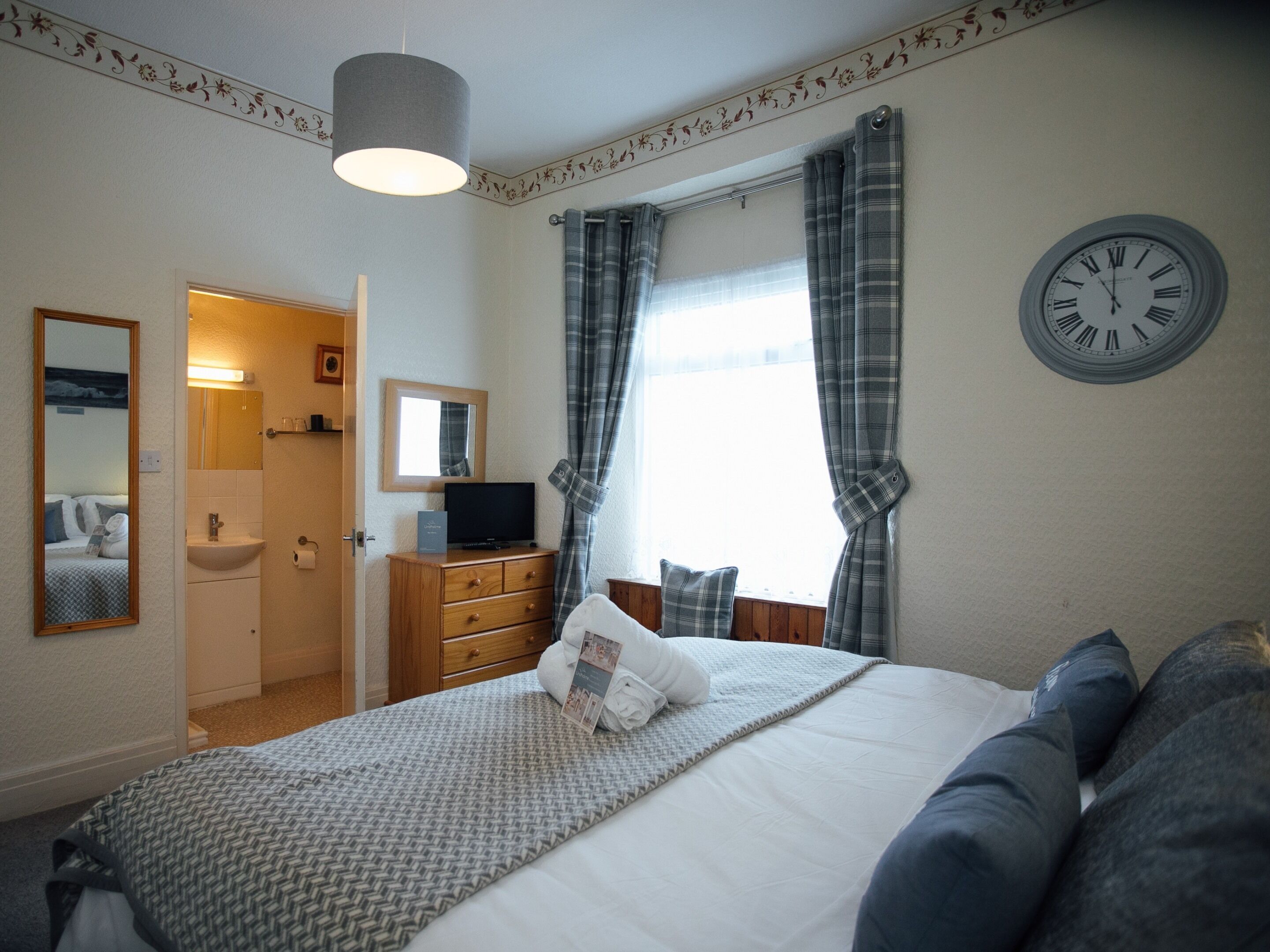 A bedroom with a bed, a dresser, a mirror, a clock, and a window with curtains.