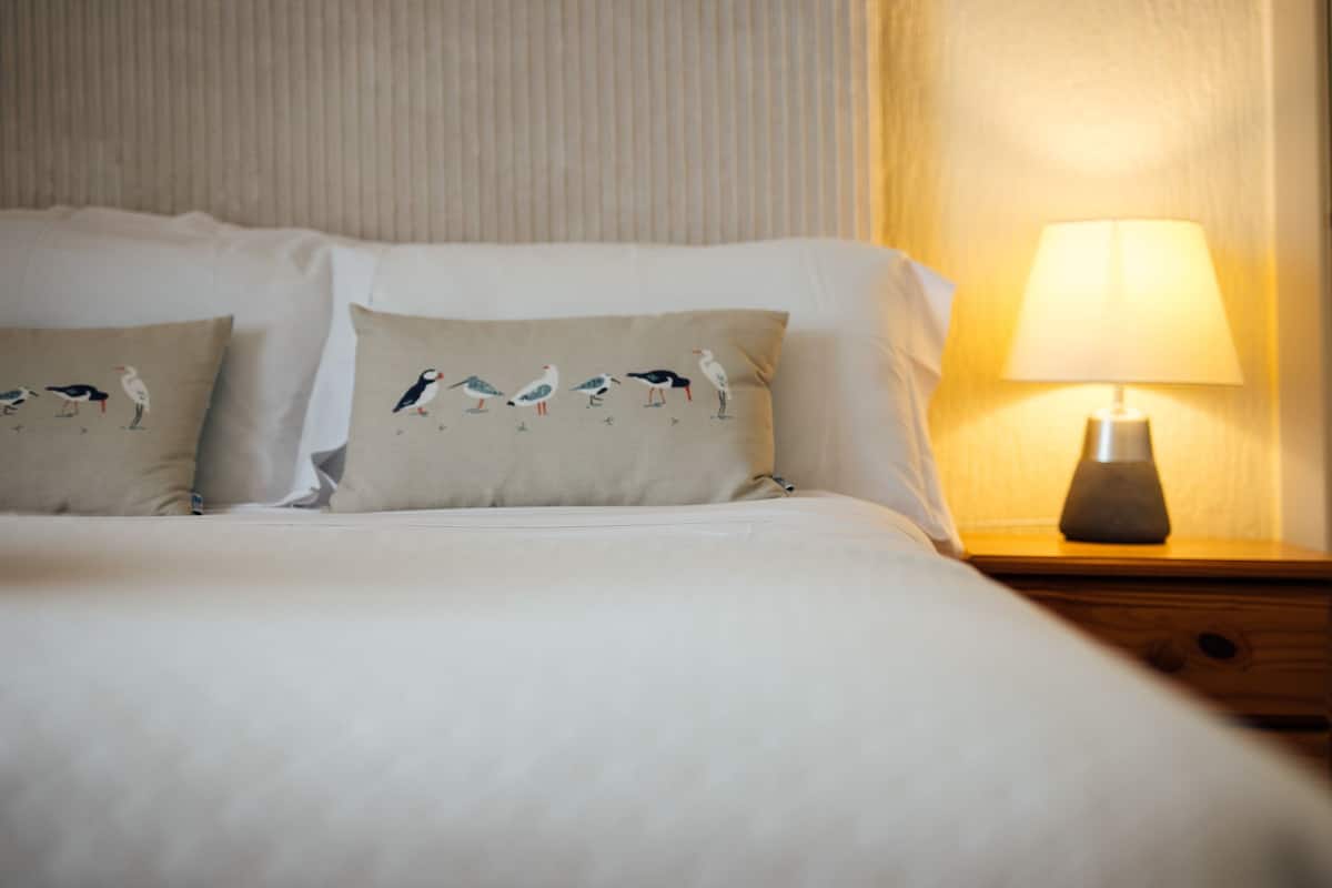 A neatly made bed with two pillows, each featuring bird designs, and a bedside table with a lamp.