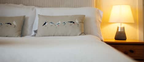 A neatly made bed with two pillows, each featuring bird designs, and a bedside table with a lamp.