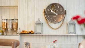 Un interior rústico con una pared de madera, un reloj de pared redondo y una pequeña mesa con un florero.