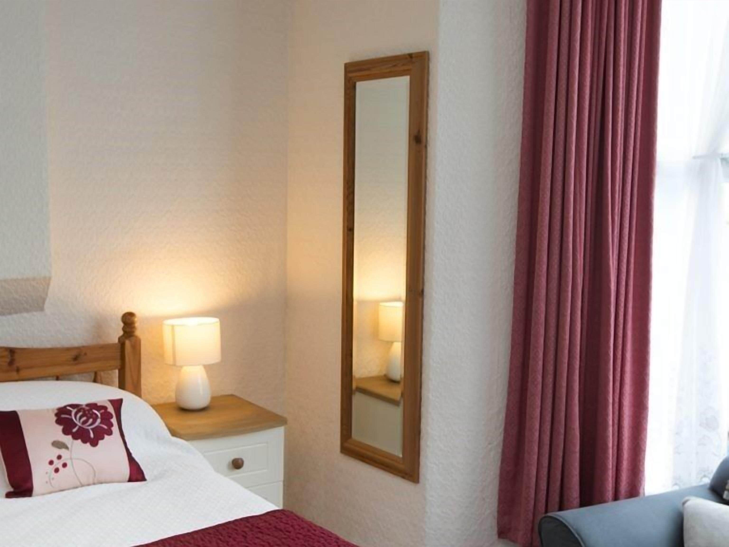 Une chambre d’hôtel comprenant un lit, une table de chevet, une lampe, un miroir et donnant sur l’extérieur.