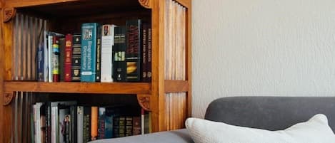 A bookshelf filled with books, a grey sofa, and a white pillow.