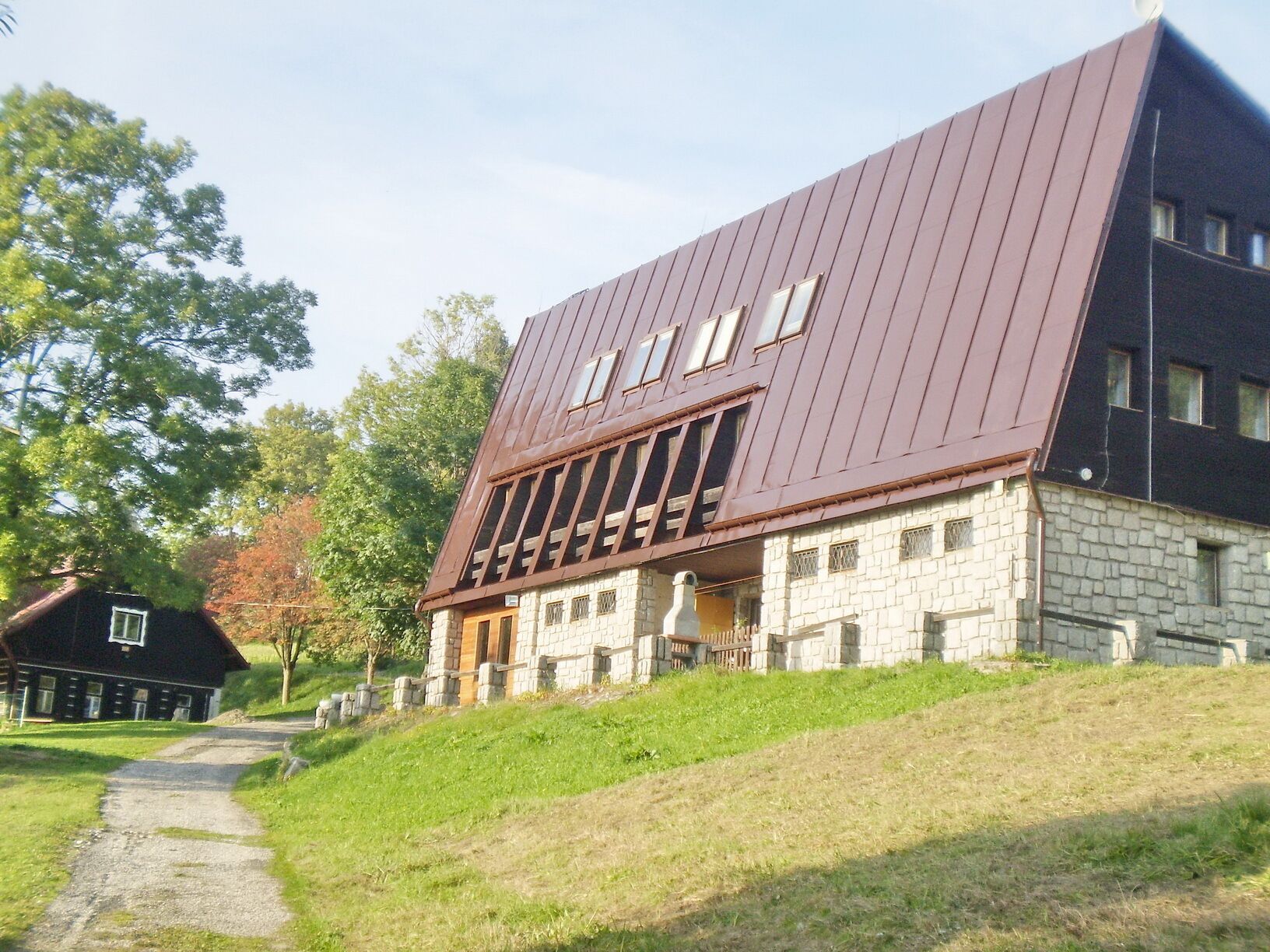 A modern building with a sloped roof and stone facade, featuring large windows and a pathway leading to the entrance.