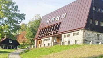 A modern building with a sloped roof and stone facade, featuring large windows and a pathway leading to the entrance.