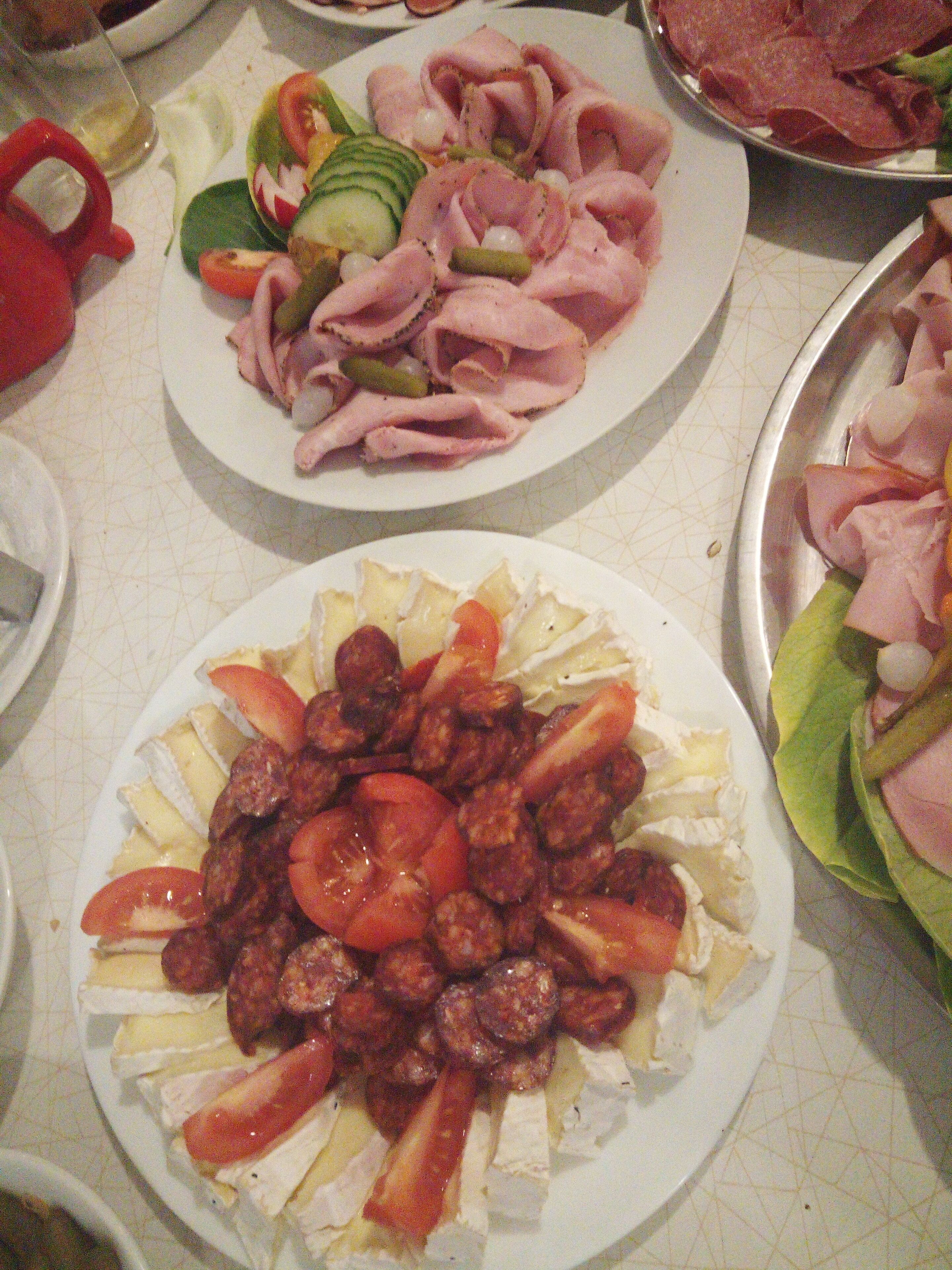 A table with various plates of food, including sliced meats, cheeses, and vegetables.