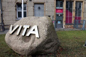 A large stone with the letters "VITA" carved into it, placed on grass in front of a building with a sign that reads "VITA." - Hotel Vita Berlin (Berlin)