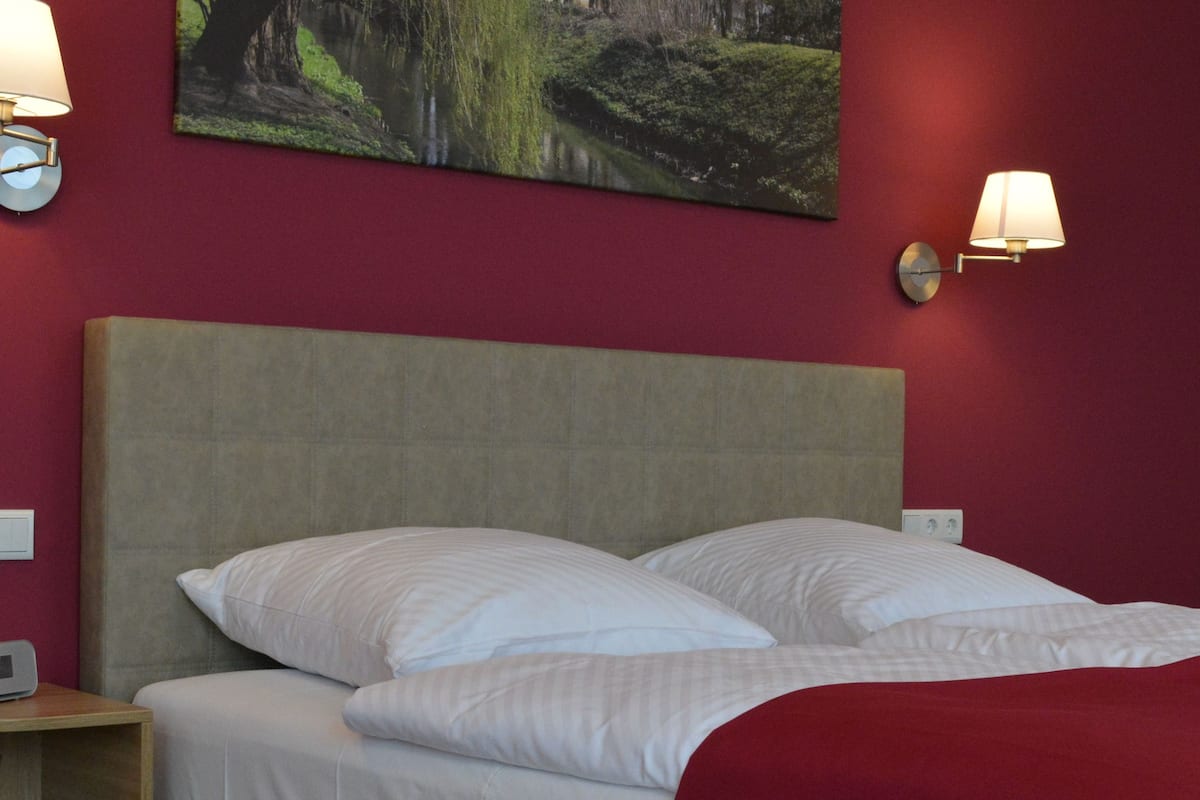A hotel room with a bed, two wall-mounted lamps, and a painting on the wall.