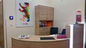 A reception desk with a wooden finish, a framed poster of a colorful bear, and a sign for 'Aktion Mensch'. - Hotel Vita Berlin (Berlin)