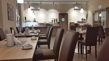 Un ristorante con un lungo tavolo da pranzo, diverse sedie e un'area cucina sullo sfondo.