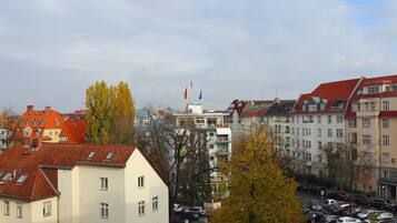 A row of multi-story buildings with red roofs and balconies, a parking lot with cars, and autumn-colored trees.