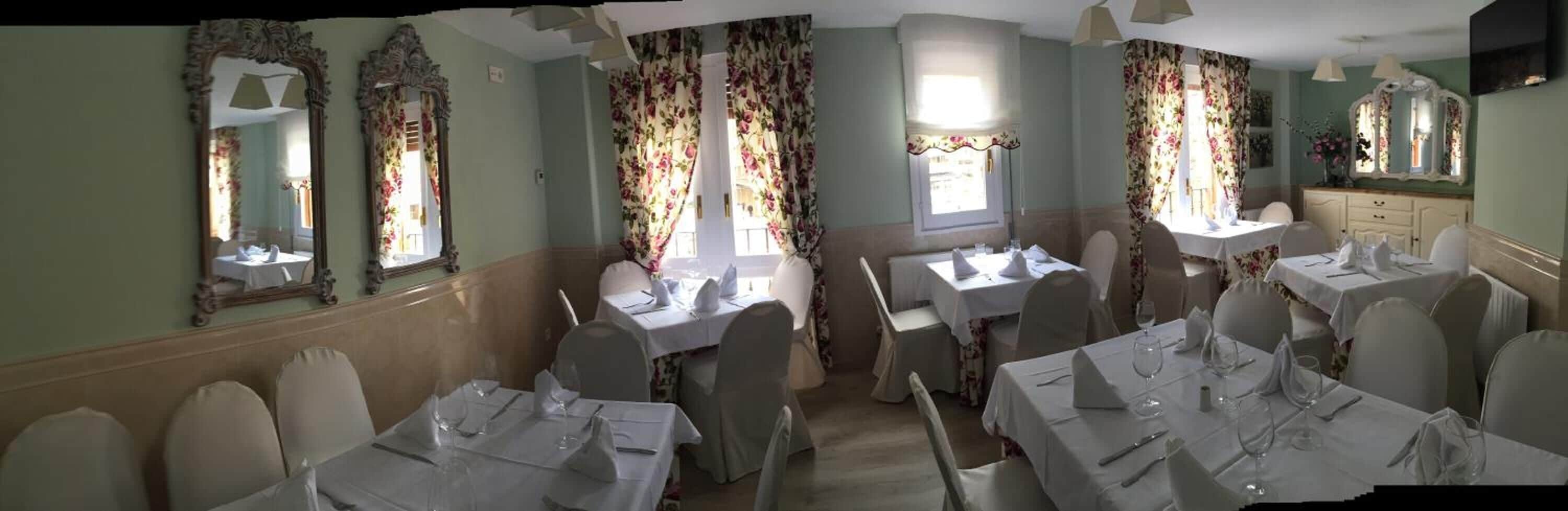 A dining area with tables set for a meal, floral curtains, and ornate mirrors on the walls.