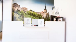 A reception desk with a framed cityscape photo, a welcome sign, and a brochure stand. - Hostal Docar (Lerma)