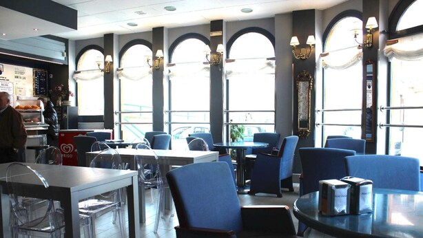 A restaurant interior with clear glass tables and blue chairs, large windows with arched tops, and a visible menu board. - Hostal Docar (Lerma)