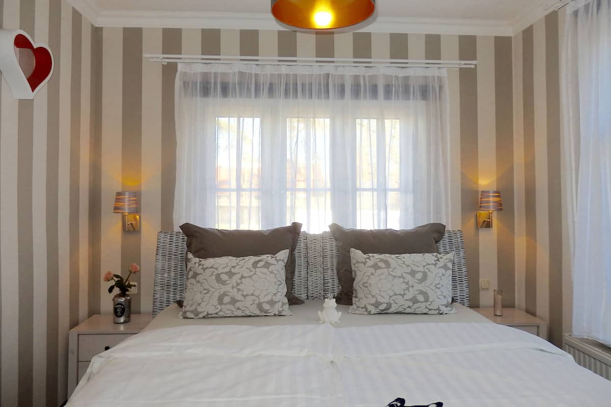 A hotel room with a large bed, striped walls, two bedside lamps, and a window with sheer curtains.
