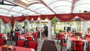 A restaurant with red chairs and white tablecloths, large windows, and a glass ceiling. - Strandhotel Villa Louisa & Appartementhäuser Villa Josephine und Christine (Breege)