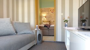 A modern living room with a grey sofa, a small side table, and a television on a white cabinet. - Strandhotel Villa Louisa & Appartementhäuser Villa Josephine und Christine (Breege)