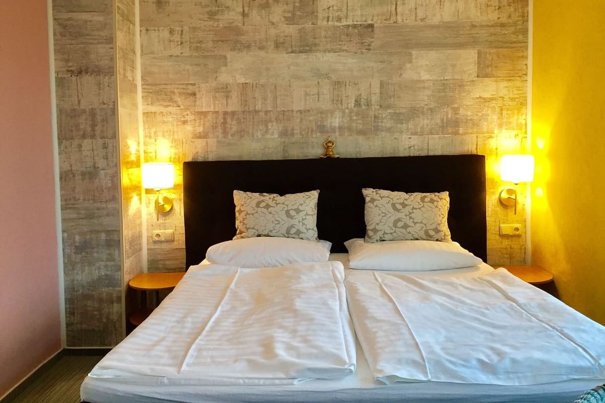 A double bed with white linens, two bedside tables, and wall-mounted lamps.
