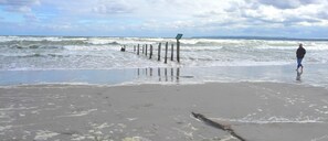 A beach with waves, a wooden structure, and a person standing. - Strandhotel Villa Louisa & Appartementhäuser Villa Josephine und Christine (Breege)