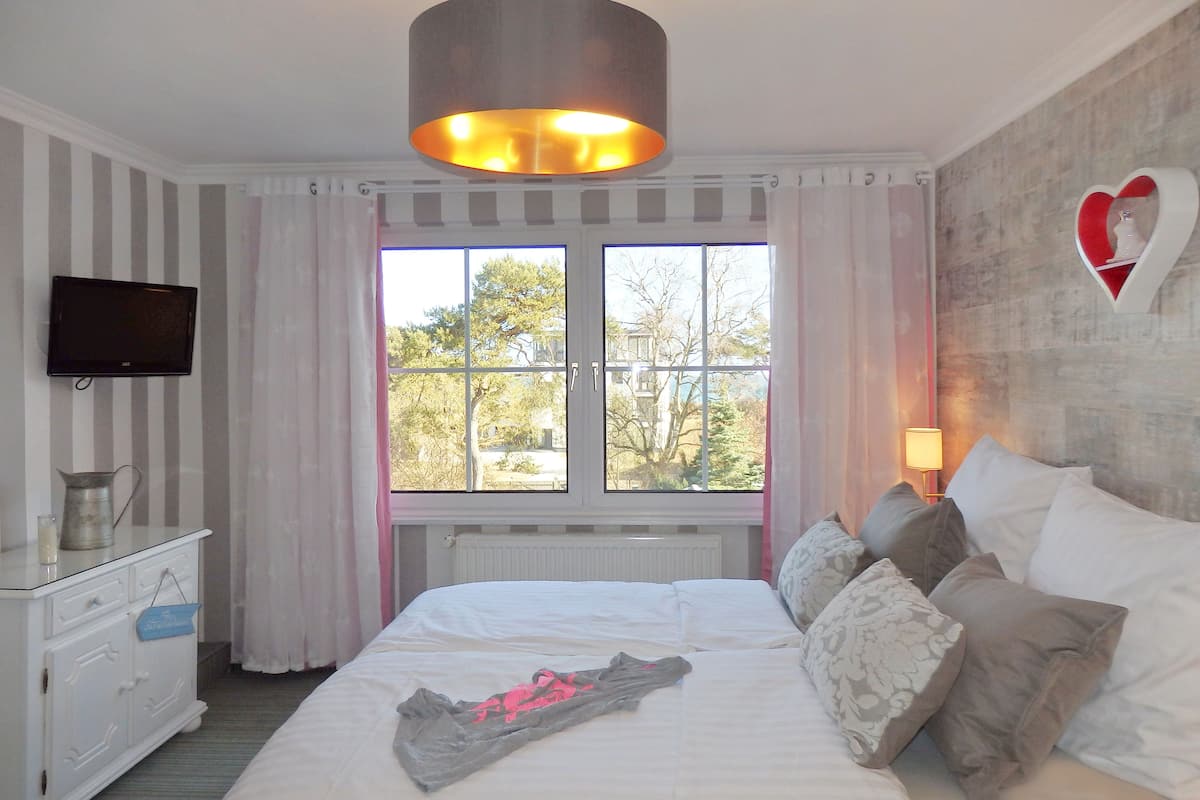 A bedroom with a bed, a TV, a dresser, and a window with a view of trees.