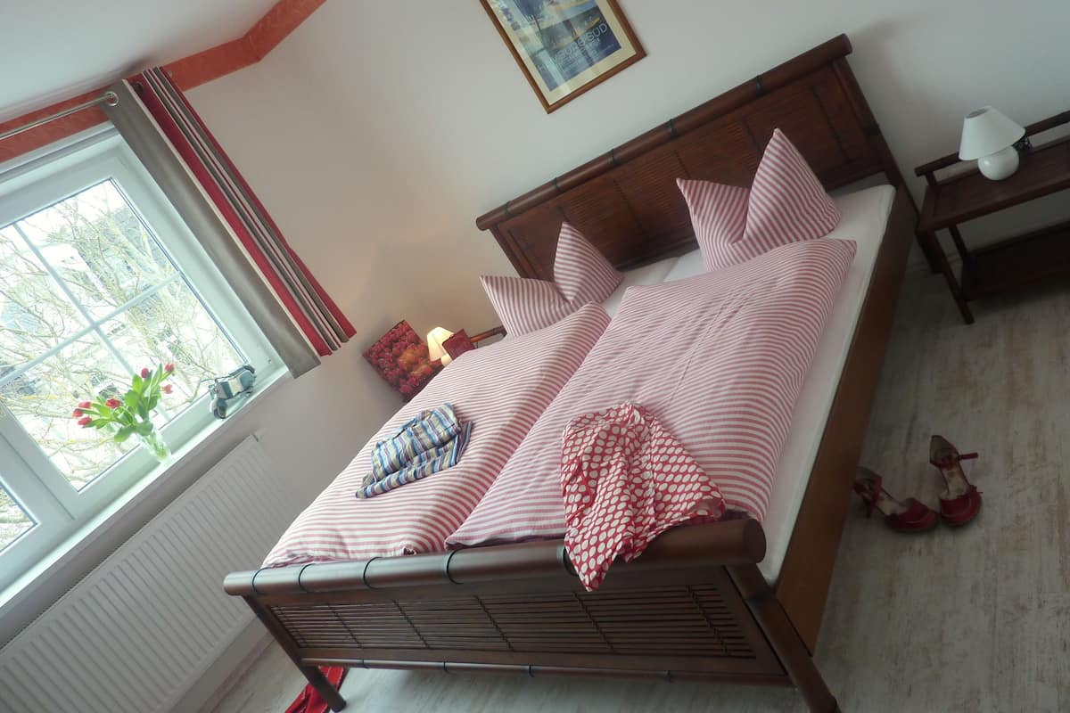 A neatly made bed with striped bedding, a wooden headboard, and a window with curtains.