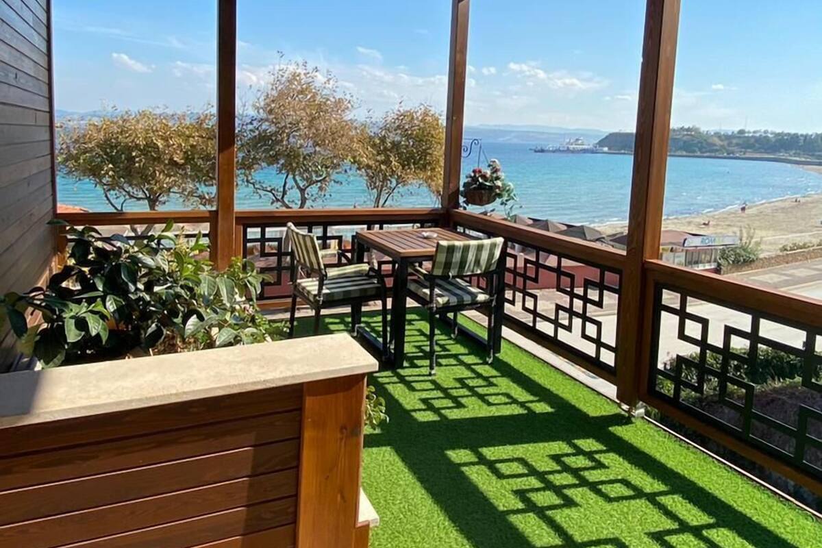 A covered outdoor seating area with a view of the sea and a beach.