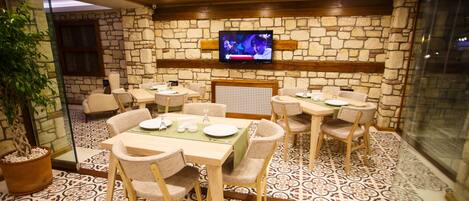 A restaurant with stone walls, wooden ceiling, and patterned floor tiles. Tables and chairs are arranged for dining.