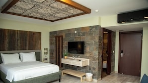 A bedroom with a bed, a TV, a stone wall, a wooden bench, and a door. - Tas Konak Boutique Hotel (Gallipoli)