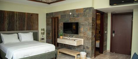 Un dormitorio con cama, televisión, pared de piedra, banco de madera y una puerta.