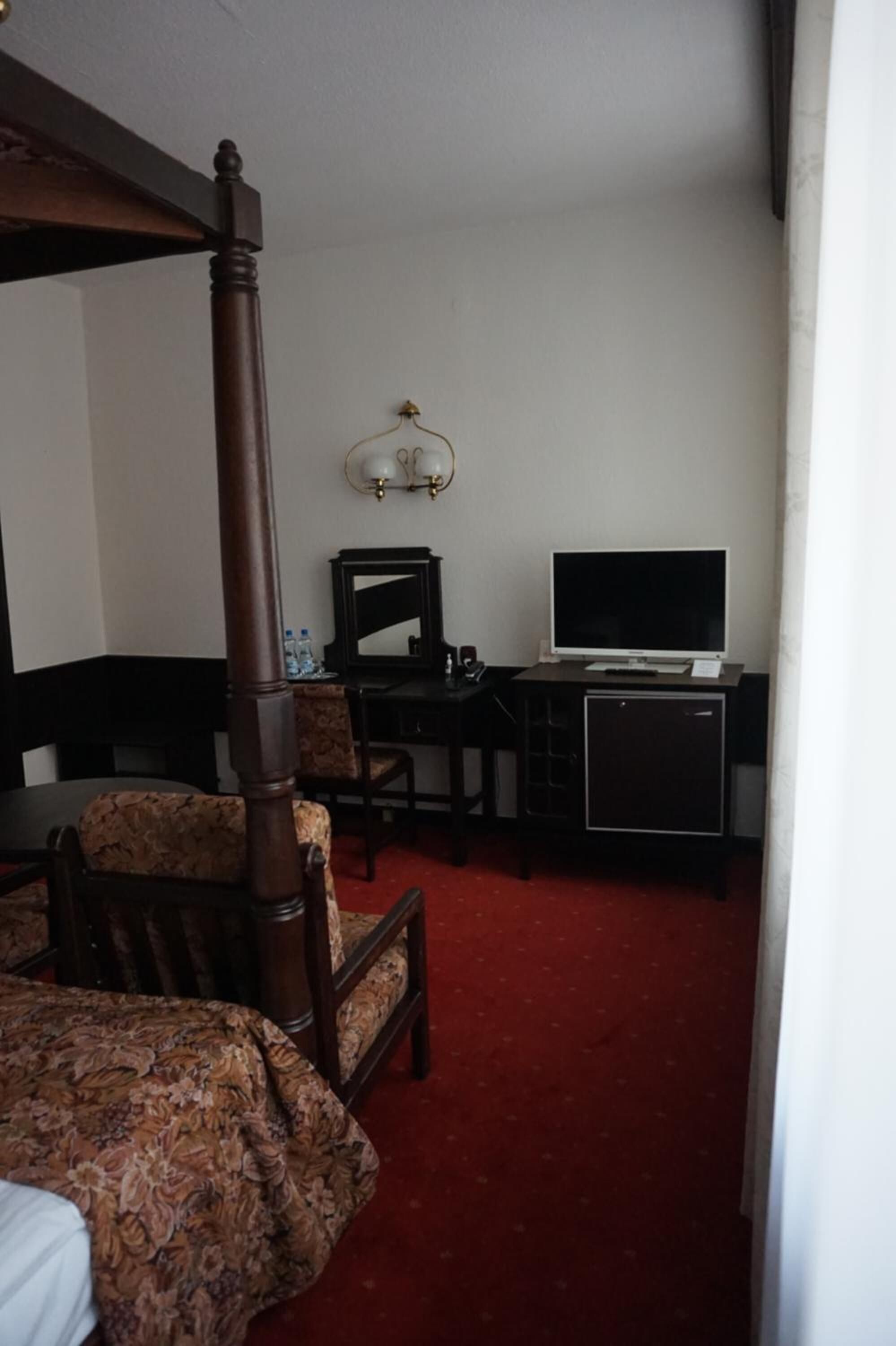 Une chambre d’hôtel avec un lit à baldaquin, un bureau avec un ordinateur, une télévision et un petit meuble de rangement.