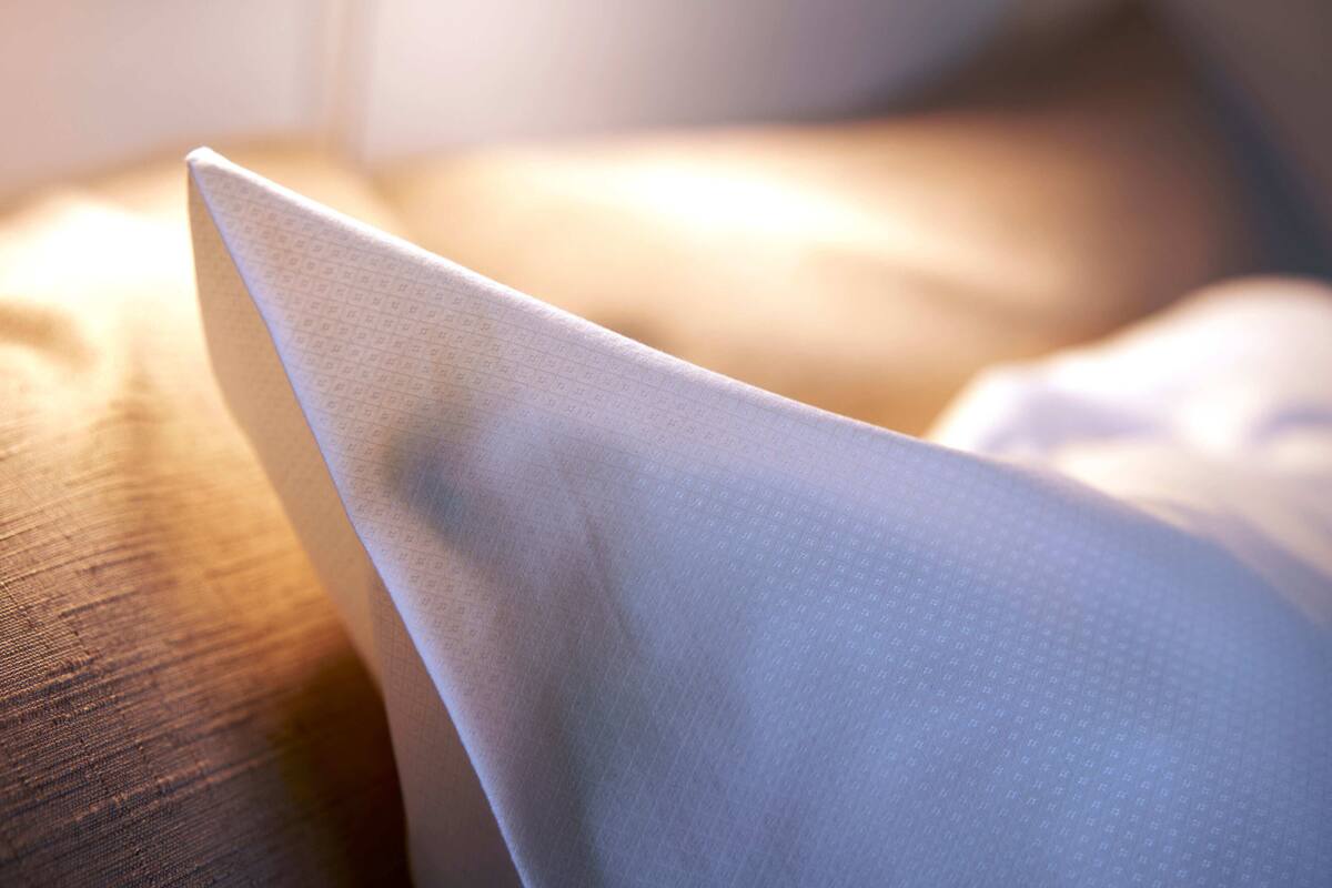 A close-up of a white fabric with a subtle pattern, likely a pillow or cushion, on a wooden surface.