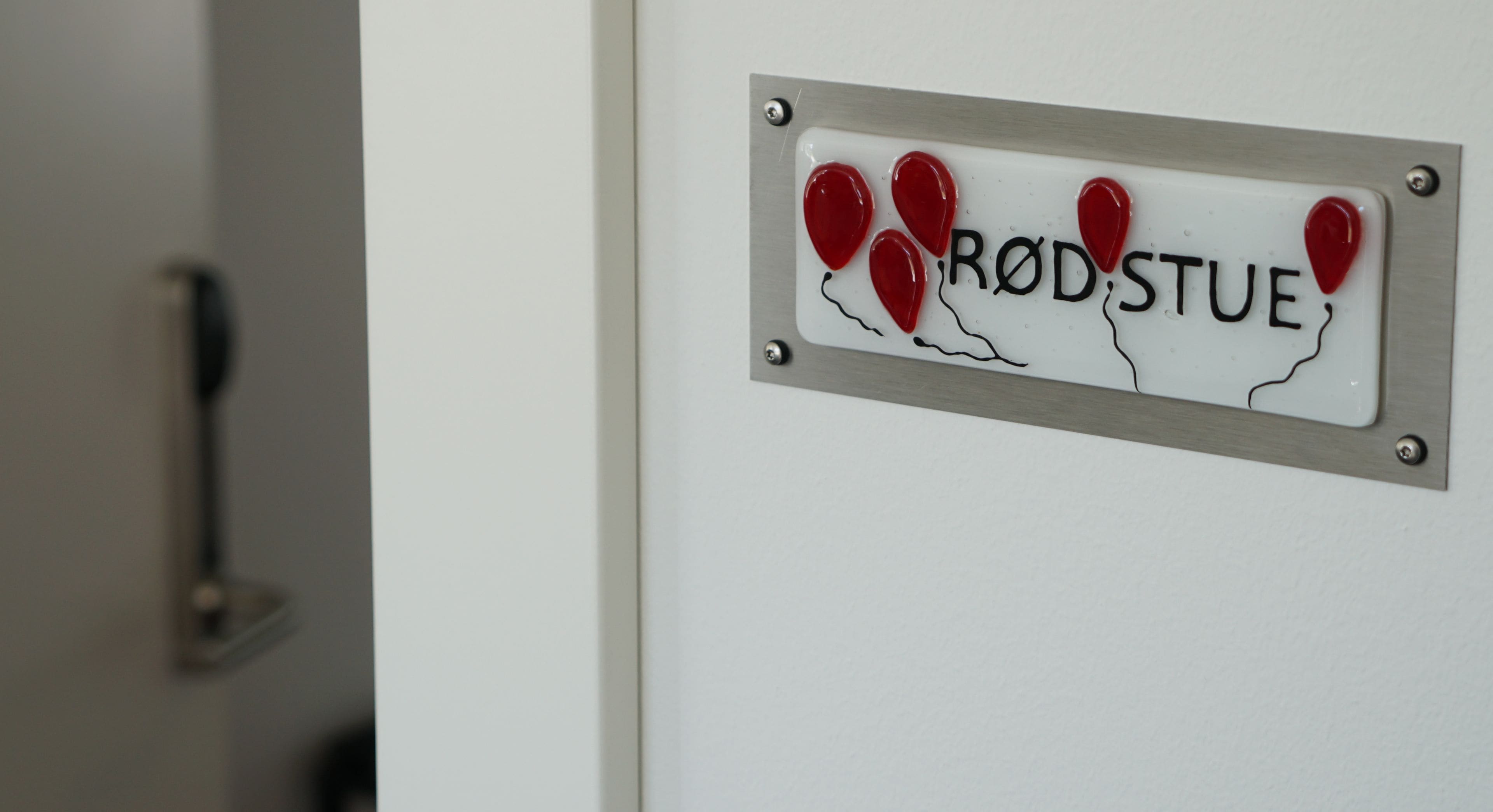 Una porta con un cartello che riporta la scritta "RØD STUE" e decorazioni a forma di cuore rosso.