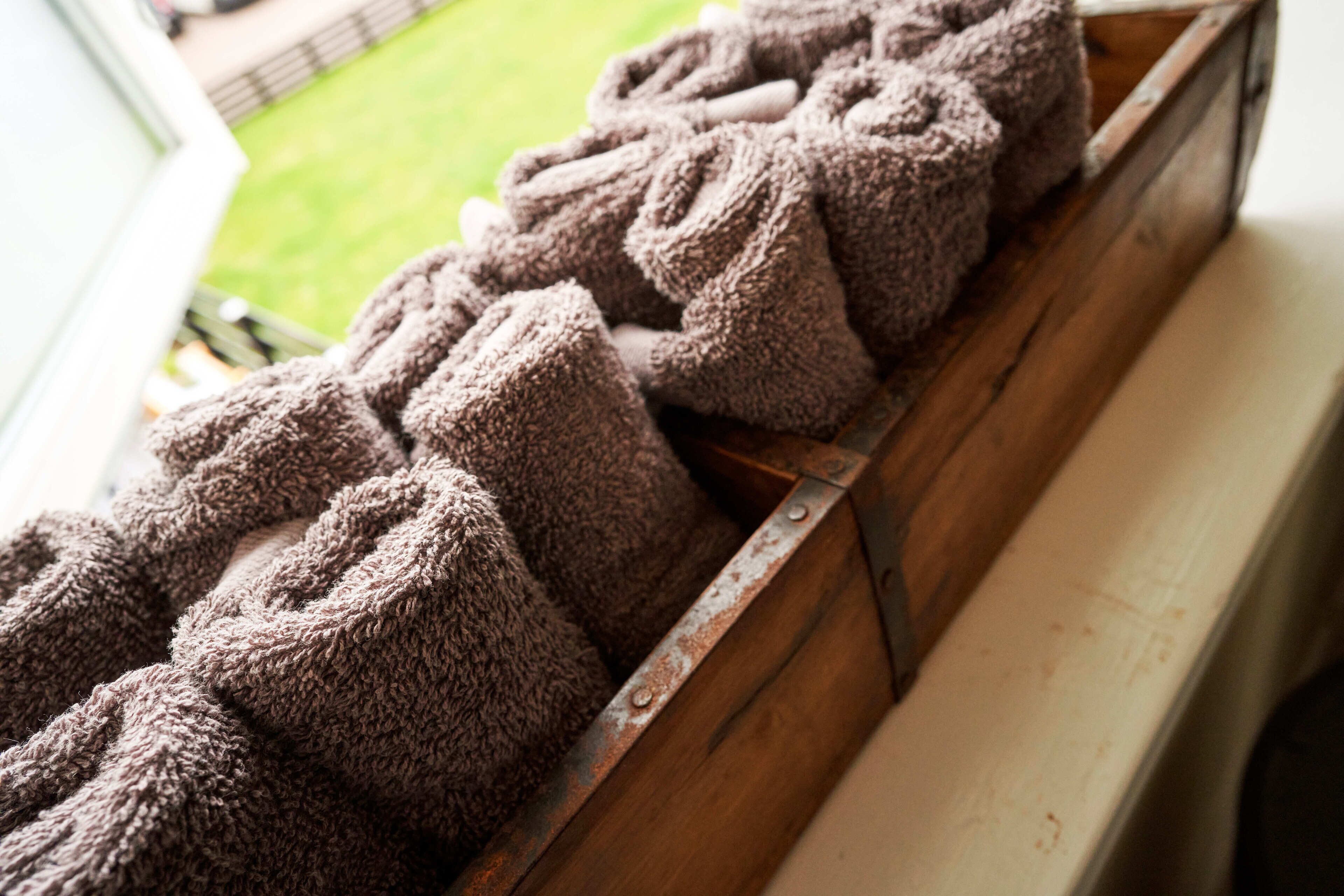 A wooden bench with a metal railing, holding several rolled-up towels.