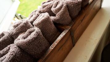A wooden bench with a metal railing, holding several rolled-up towels.