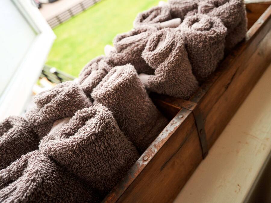 A wooden bench with a metal railing, holding several rolled-up towels.