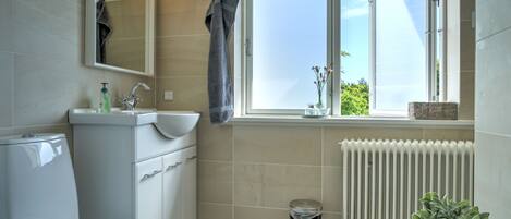 A modern bathroom with a toilet, sink, mirror, and window.