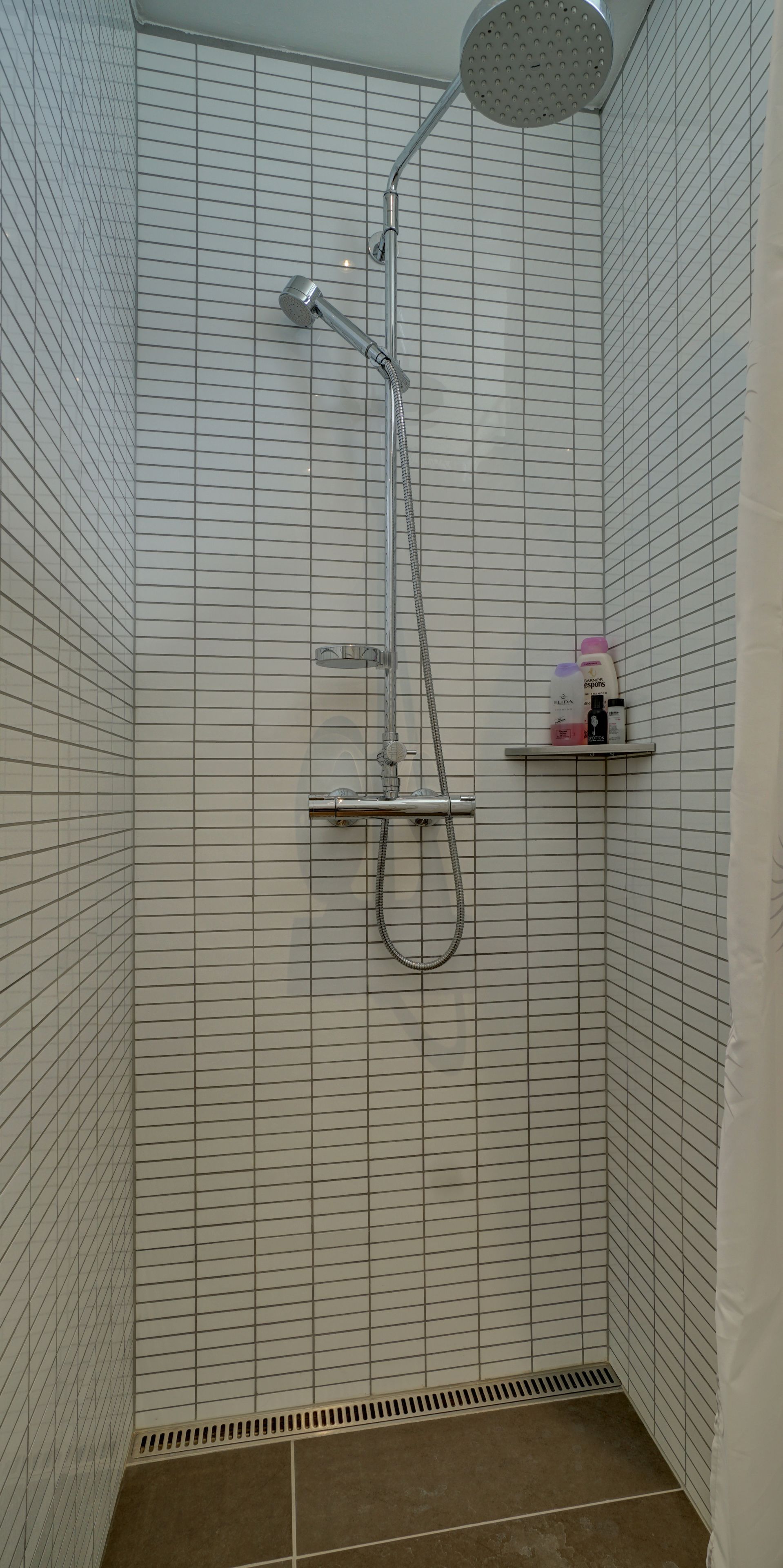 A shower with a handheld showerhead, a wall-mounted faucet, and a shelf with toiletries.