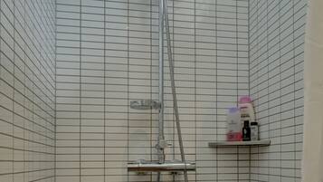 A shower with a handheld showerhead, a wall-mounted faucet, and a shelf with toiletries.