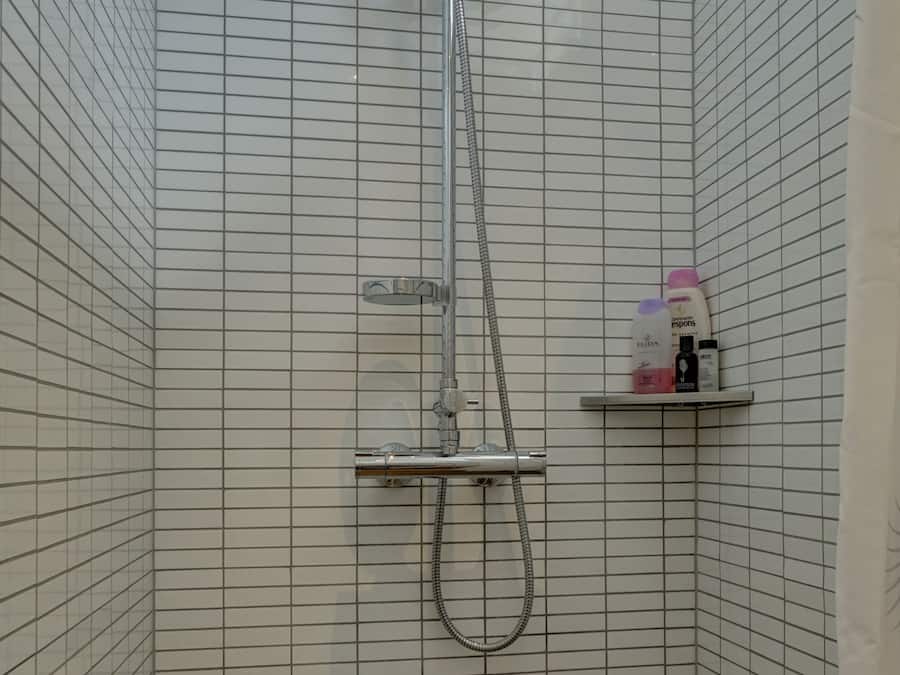Um chuveiro com um chuveiro de mão, uma torneira fixada na parede e uma prateleira com produtos de higiene pessoal.
