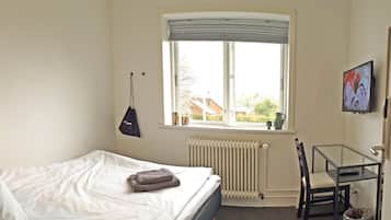 Un dormitorio con cama, ventana con vistas, radiador, una silla y un cuadro en la pared.